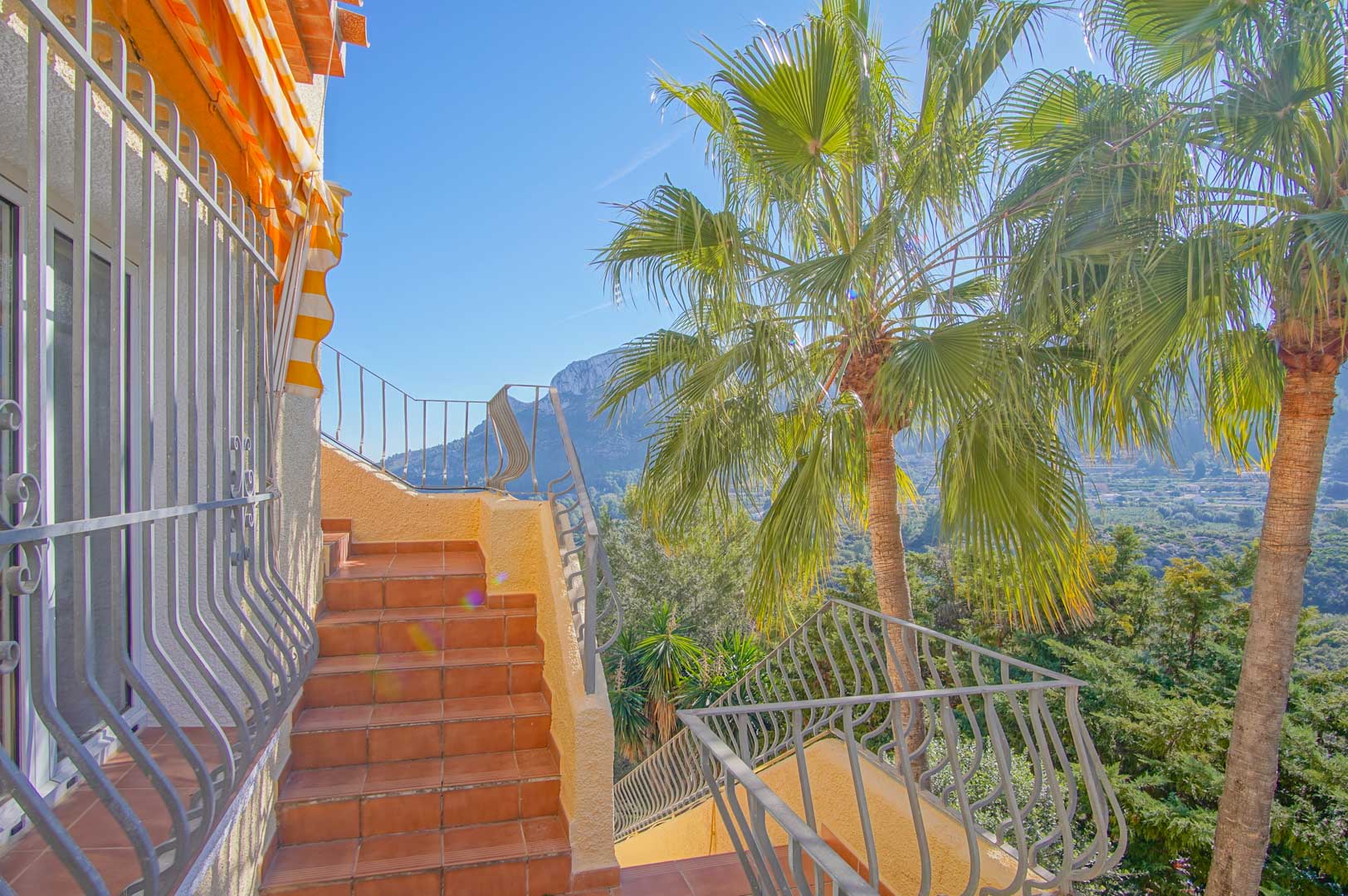 Escalera exterior de baldosas cerámicas y barandilla de hierro, con vistas a la montaña y palmeras integradas en el entorno natural de la villa.