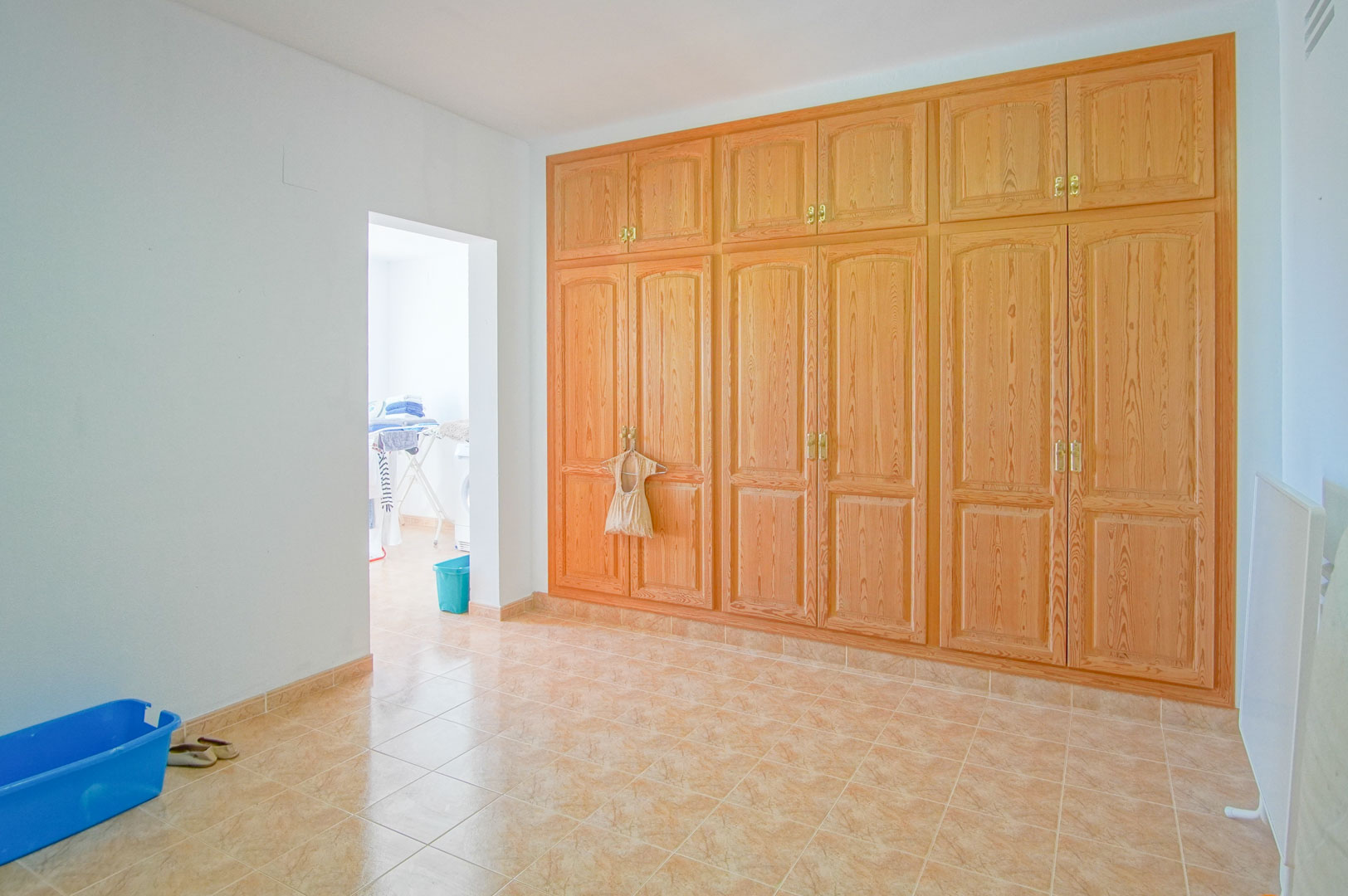 Habitación con amplio armario empotrado de madera, suelos cerámicos y acceso directo a la zona de lavandería. Espacio versátil con abundante luz natural.