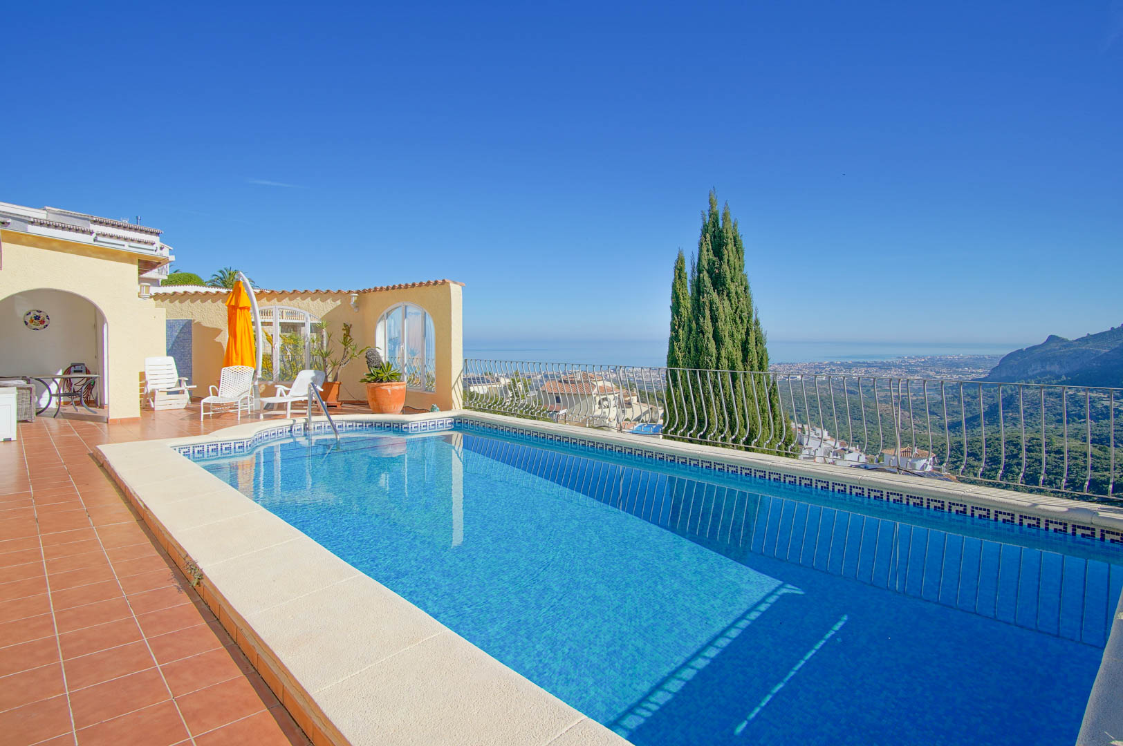 Piscina rectangular con gresite azul y amplia terraza de terracota, orientada hacia vistas panorámicas del mar Mediterráneo y el paisaje costero de Monte Pego.