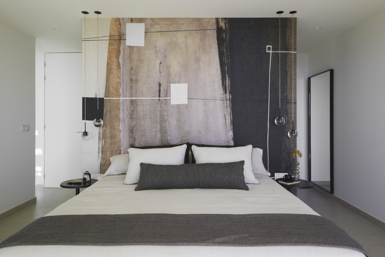 Dormitorio moderno con un mural artístico abstracto en el cabecero, luminarias colgantes de diseño y mesas auxiliares minimalistas en tonos oscuros.