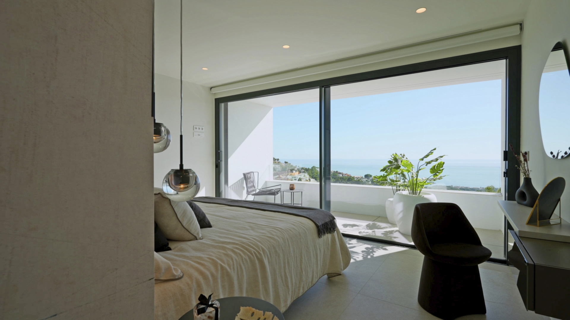 Dormitorio principal con ventanales de suelo a techo, acceso a terraza privada y vistas al mar. Incluye iluminación de diseño y mobiliario minimalista.