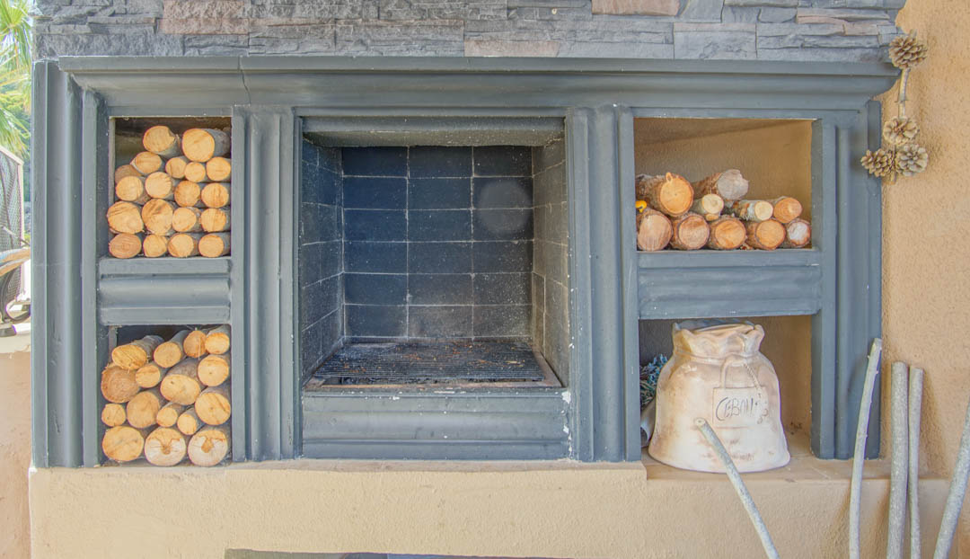 Chimenea exterior integrada con parrilla central, revestimiento de piedra y compartimentos laterales para el almacenamiento de leña.