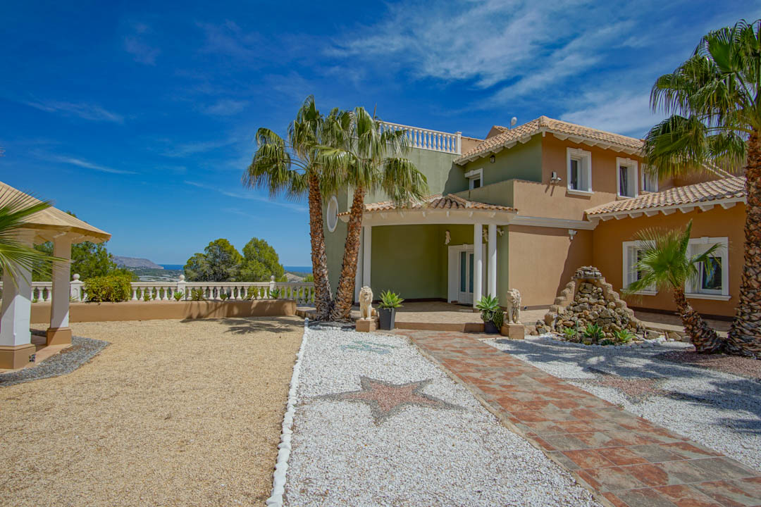 Entrada principal con mosaicos de estrellas, palmeras y vistas al mar. La fachada combina tonos tierra con columnas blancas y fuentes de piedra.