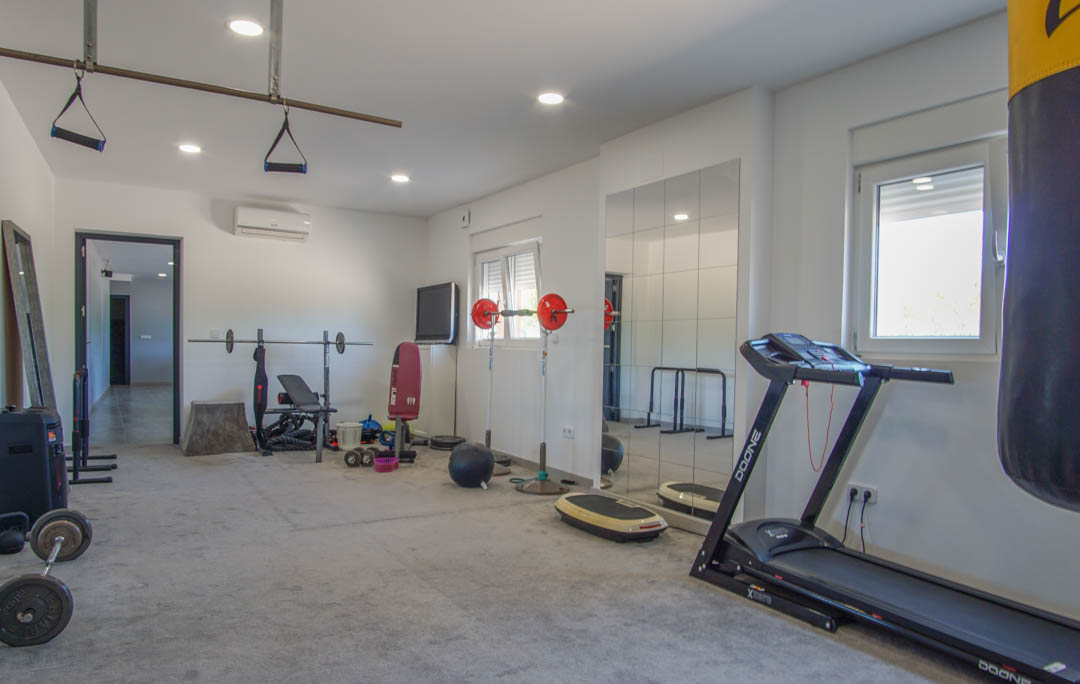 Gimnasio privado equipado con cinta de correr, saco de boxeo y pesas. Cuenta con suelo técnico, espejos de pared, iluminación empotrada y climatización.