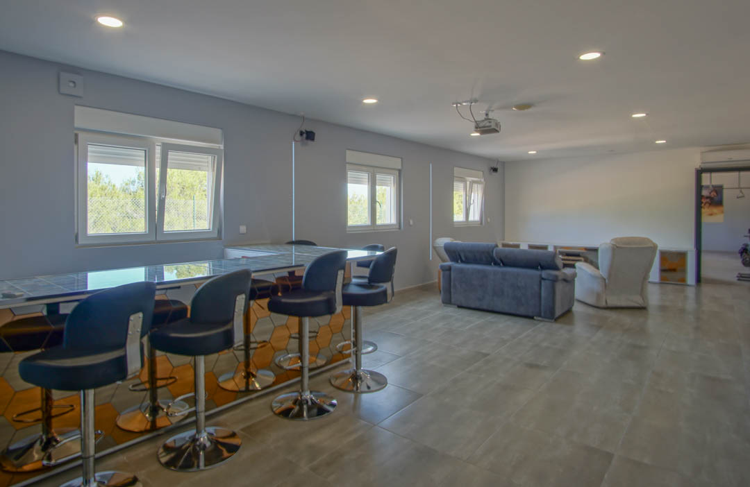 Sala de entretenimiento en la planta baja con bar integrado, zona de cine con proyector y barra con acabado geométrico de espejo.