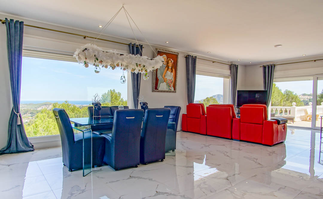 Salón comedor de planta abierta con suelos de mármol pulido, mobiliario contemporáneo y amplios ventanales que enmarcan vistas panorámicas al mar Mediterráneo.