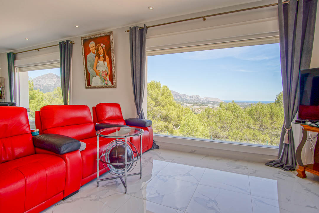 Salón luminoso con sillones de cuero rojo, suelo de mármol blanco y amplios ventanales con vistas panorámicas al mar Mediterráneo y las montañas.