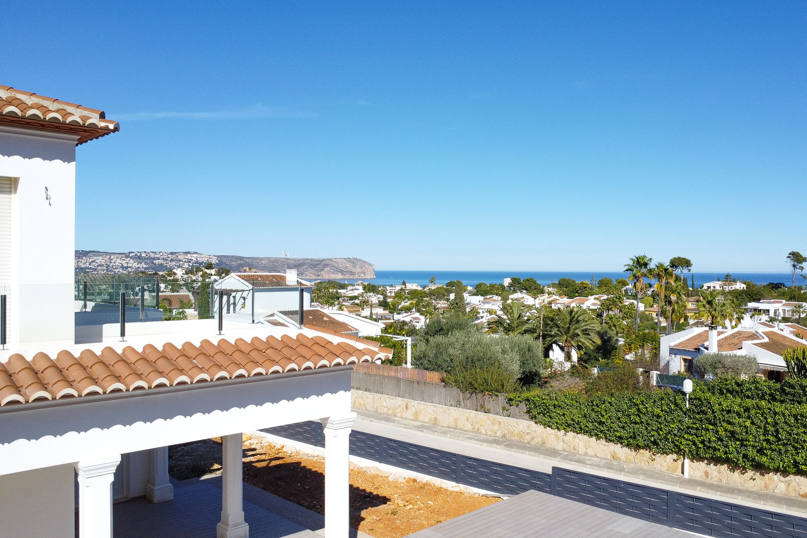 Vista panorámica al mar Mediterráneo y al cabo desde la terraza superior, destacando la arquitectura blanca con tejas cerámicas y barandillas de cristal.