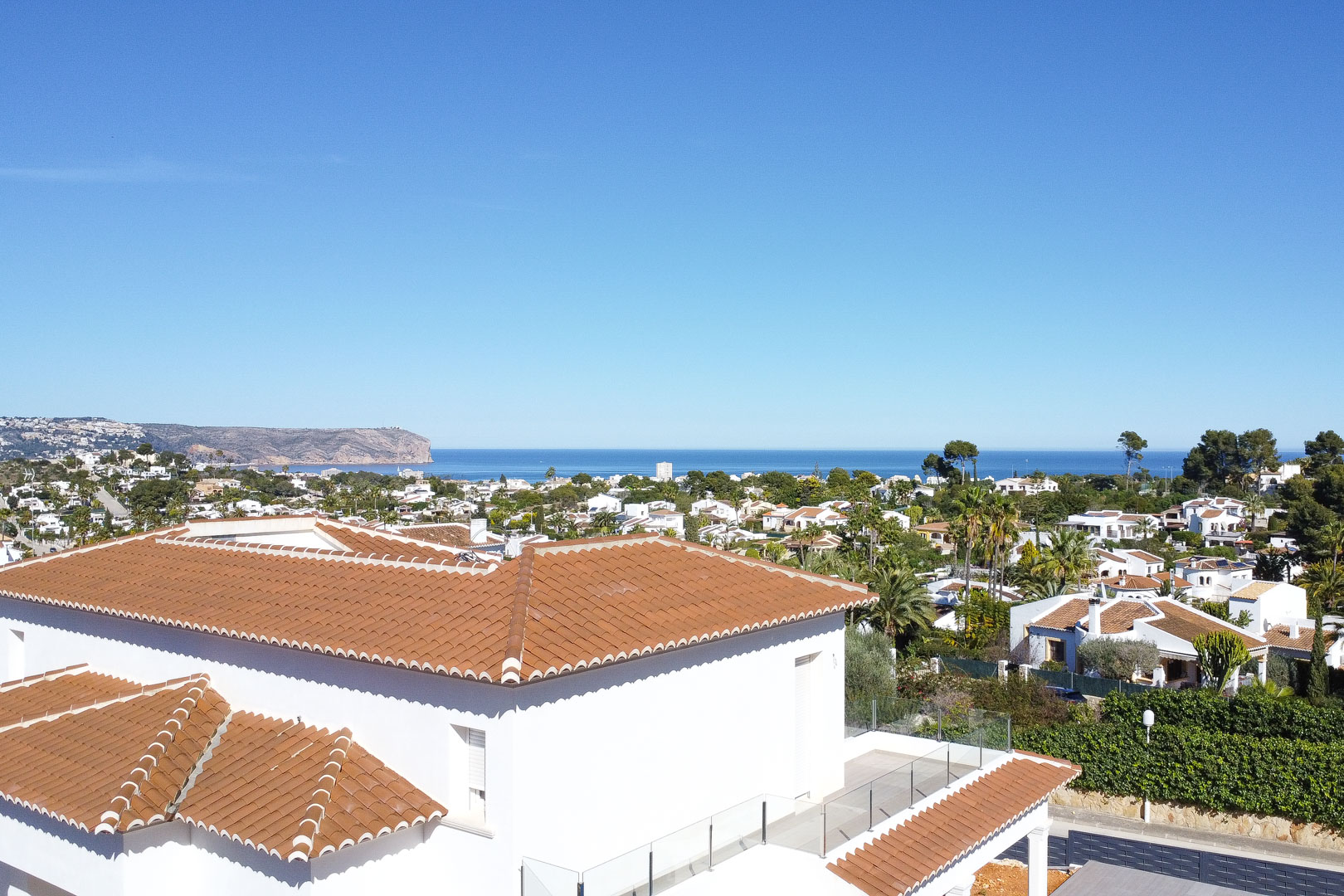 Vista panorámica desde la planta superior que muestra el tejado de teja cerámica, la terraza con barandilla de cristal y vistas despejadas al mar Mediterráneo y al cabo.