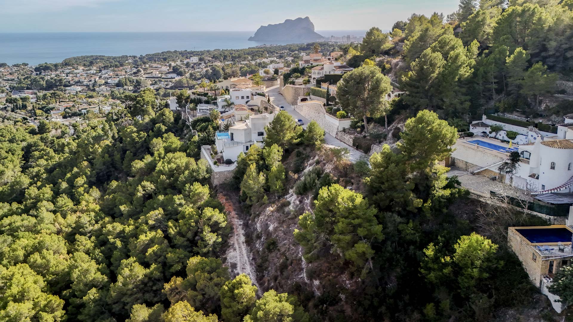 Vista aérea de la zona residencial en Benissa, mostrando la proximidad al Peñón de Ifach y la extensa zona verde protegida que rodea las parcelas.
