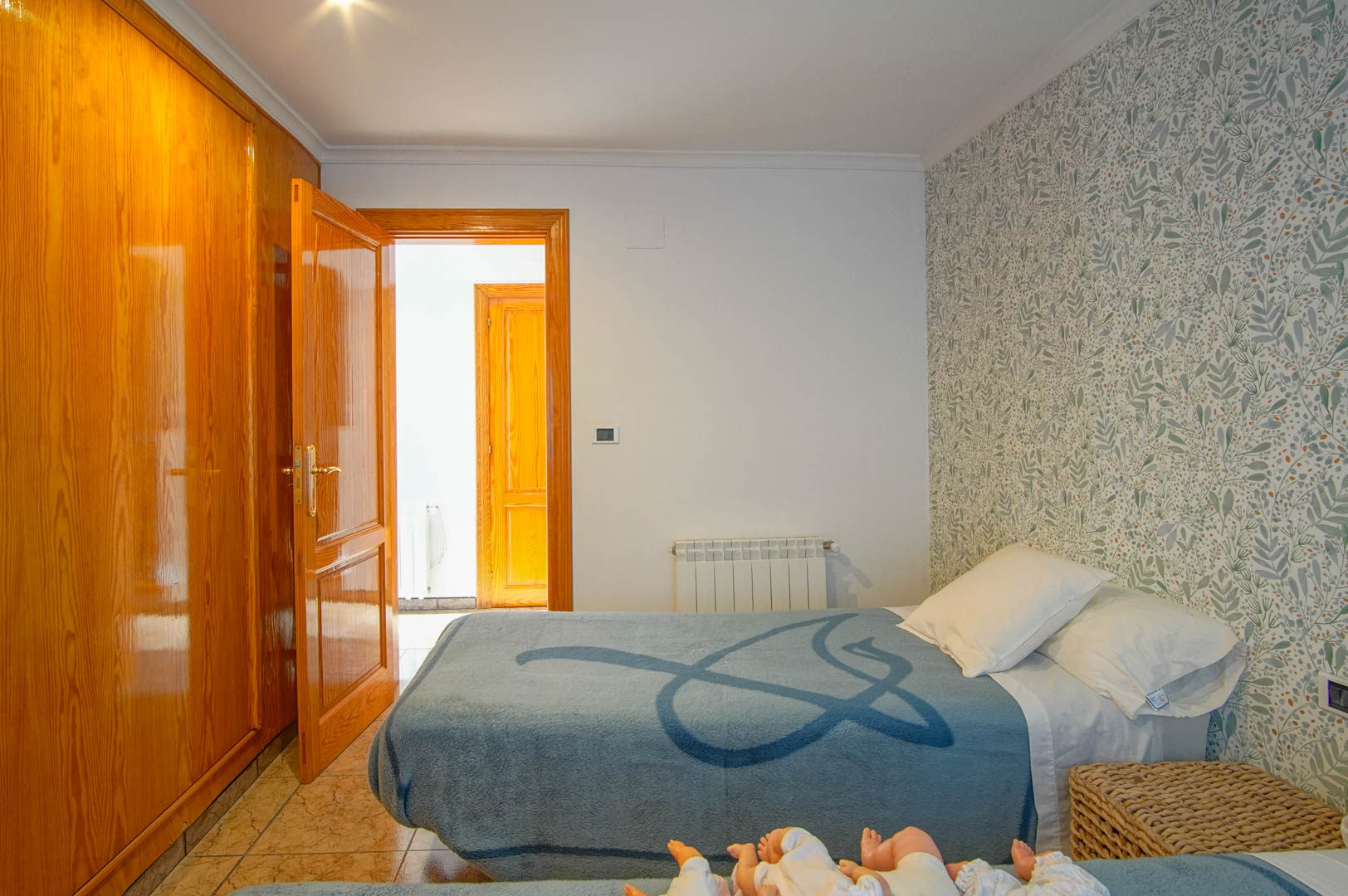 Dormitorio con armario empotrado de madera barnizada, papel pintado de motivos botánicos, suelos cerámicos y calefacción por radiador.