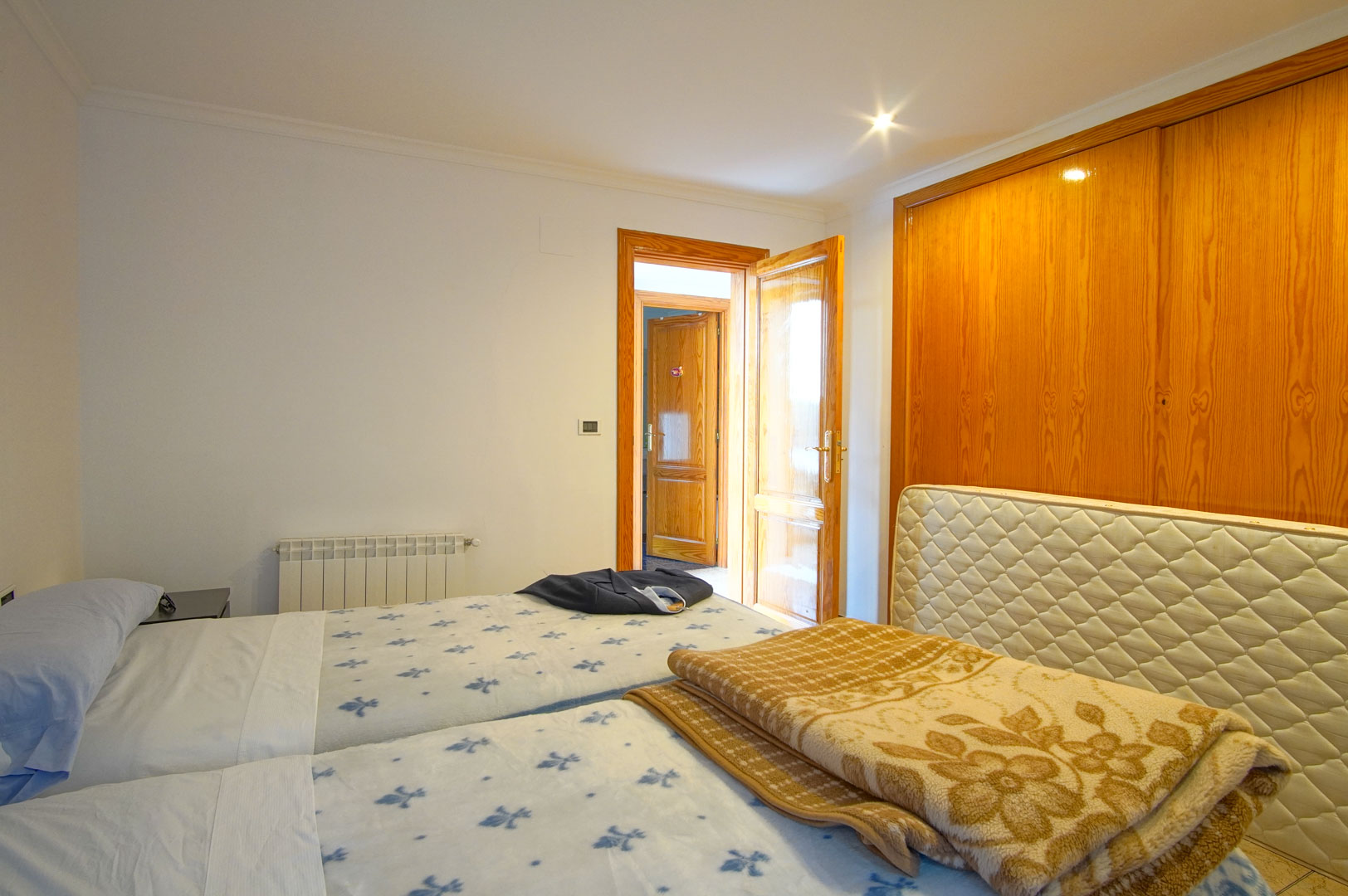 Dormitorio luminoso con armarios empotrados de madera, dos camas individuales y calefacción por radiador. Las puertas de madera maciza aportan calidez al espacio.
