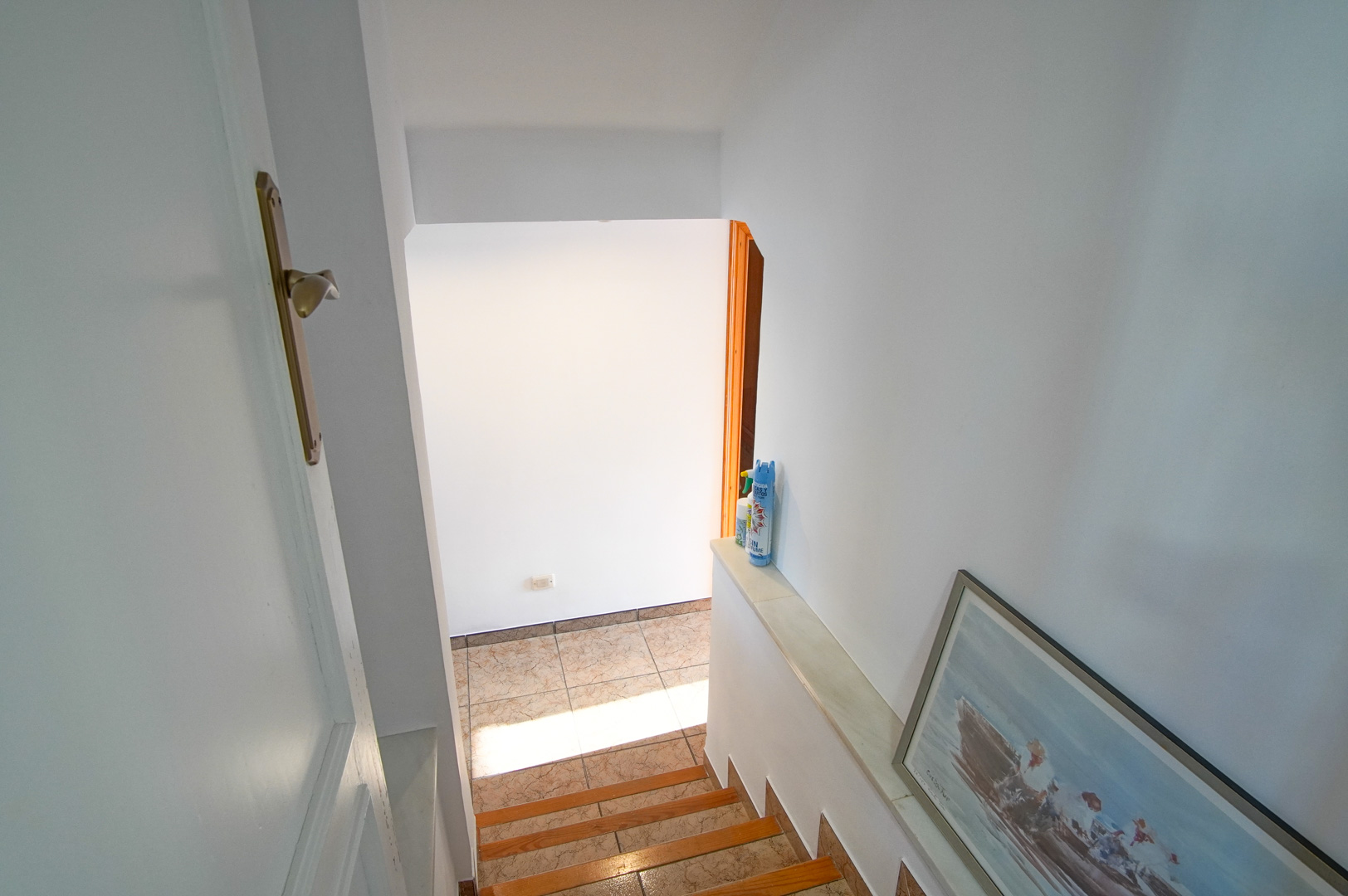 Escalera interior con peldaños en madera y cerámica, rodeada de paredes blancas que realzan la luminosidad natural hacia los niveles inferiores.