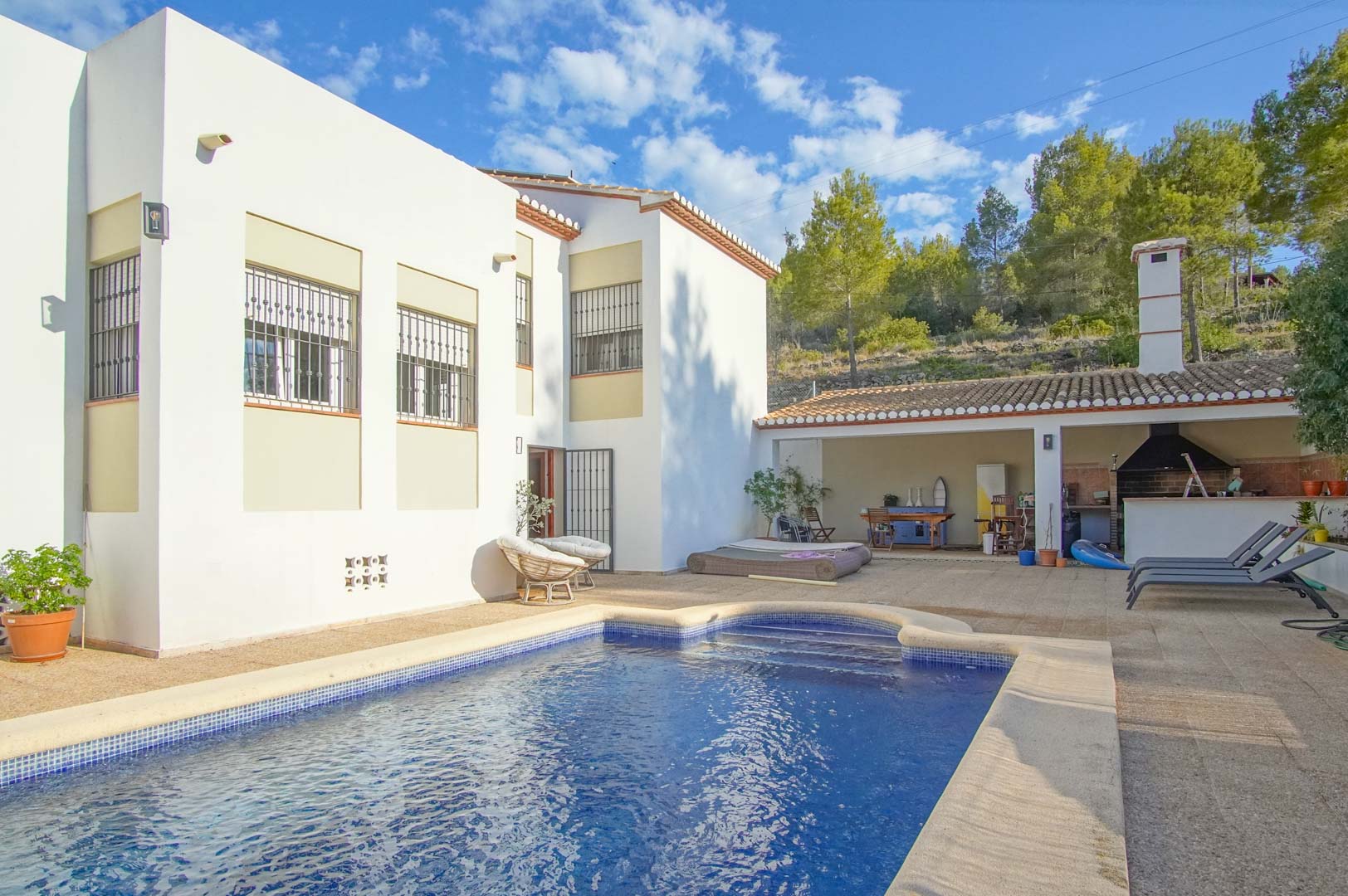 Exterior con piscina privada, amplia terraza y zona de barbacoa cubierta, rodeada por el entorno natural de pinos del Montgó en Las Rotas.