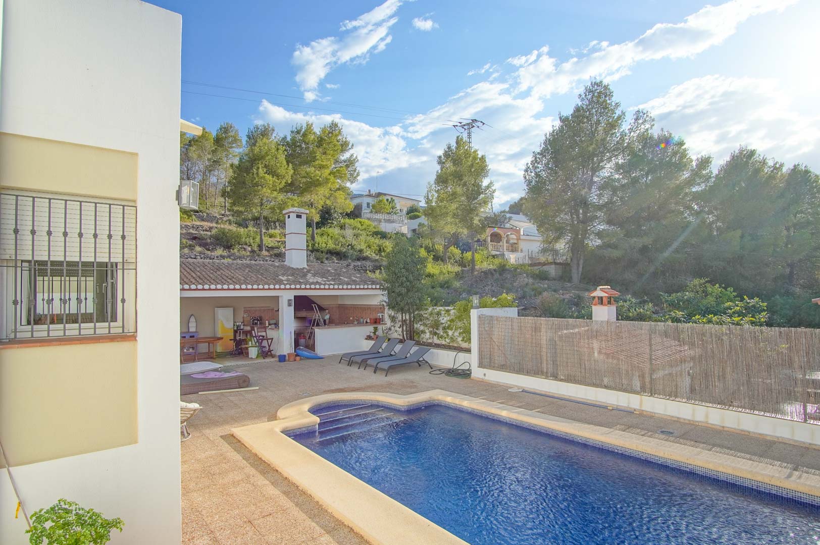 Piscina privada rodeada de una amplia terraza de piedra, con zona de barbacoa cubierta y vistas a la ladera arbolada del Parque Natural del Montgó.