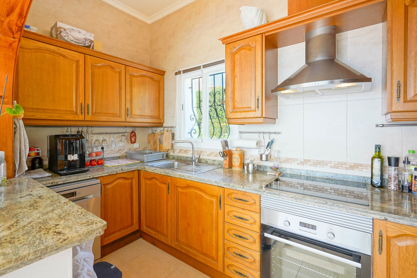 Cocina semiabierta con armarios de madera clásica, encimeras de granito y electrodomésticos de acero inoxidable, incluyendo campana extractora y horno integrado.