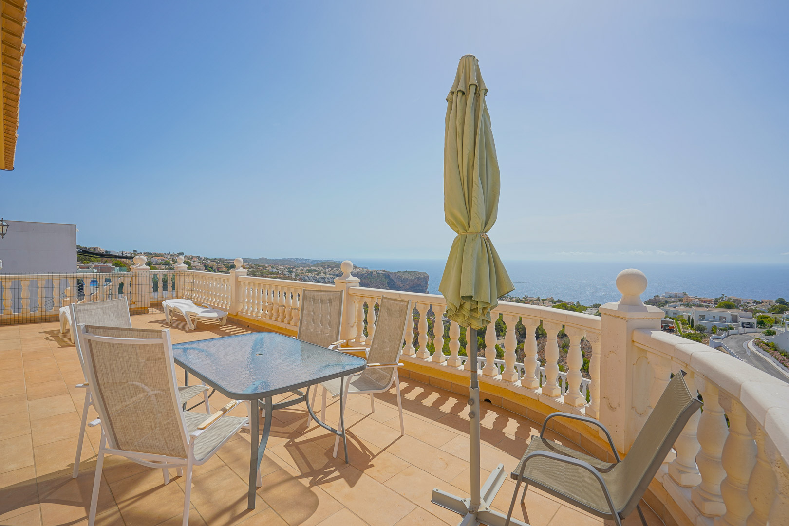 Terraza superior con mesa de cristal, sillas de exterior y balaustrada blanca, ofreciendo vistas panorámicas al mar Mediterráneo y los acantilados de Cumbre del Sol.