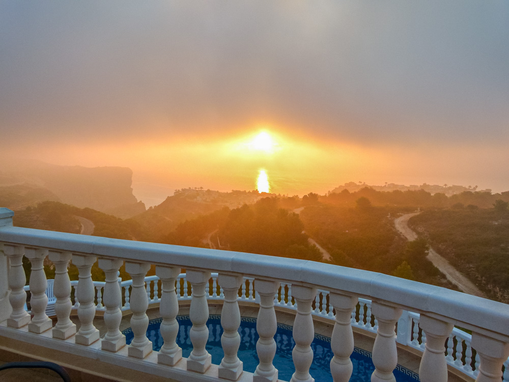 Vista desde la terraza con balaustrada blanca hacia la piscina y el atardecer sobre los acantilados costeros de Cumbre del Sol.