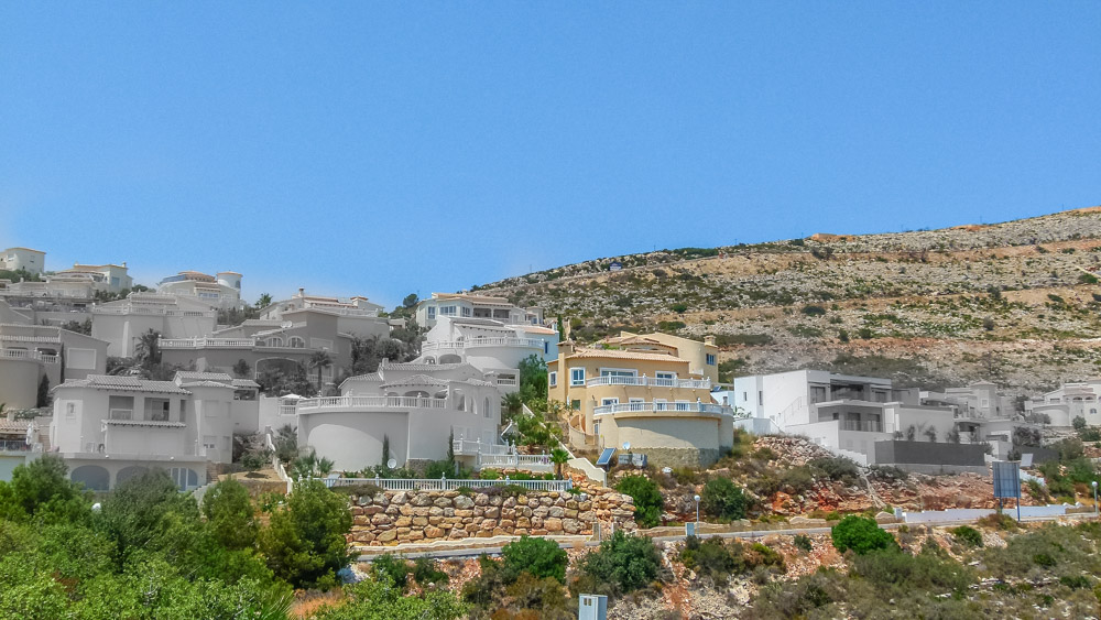 Vista panorámica de villas blancas escalonadas en la ladera de Cumbre del Sol, con muros de piedra natural y terrazas curvas bajo un cielo despejado.