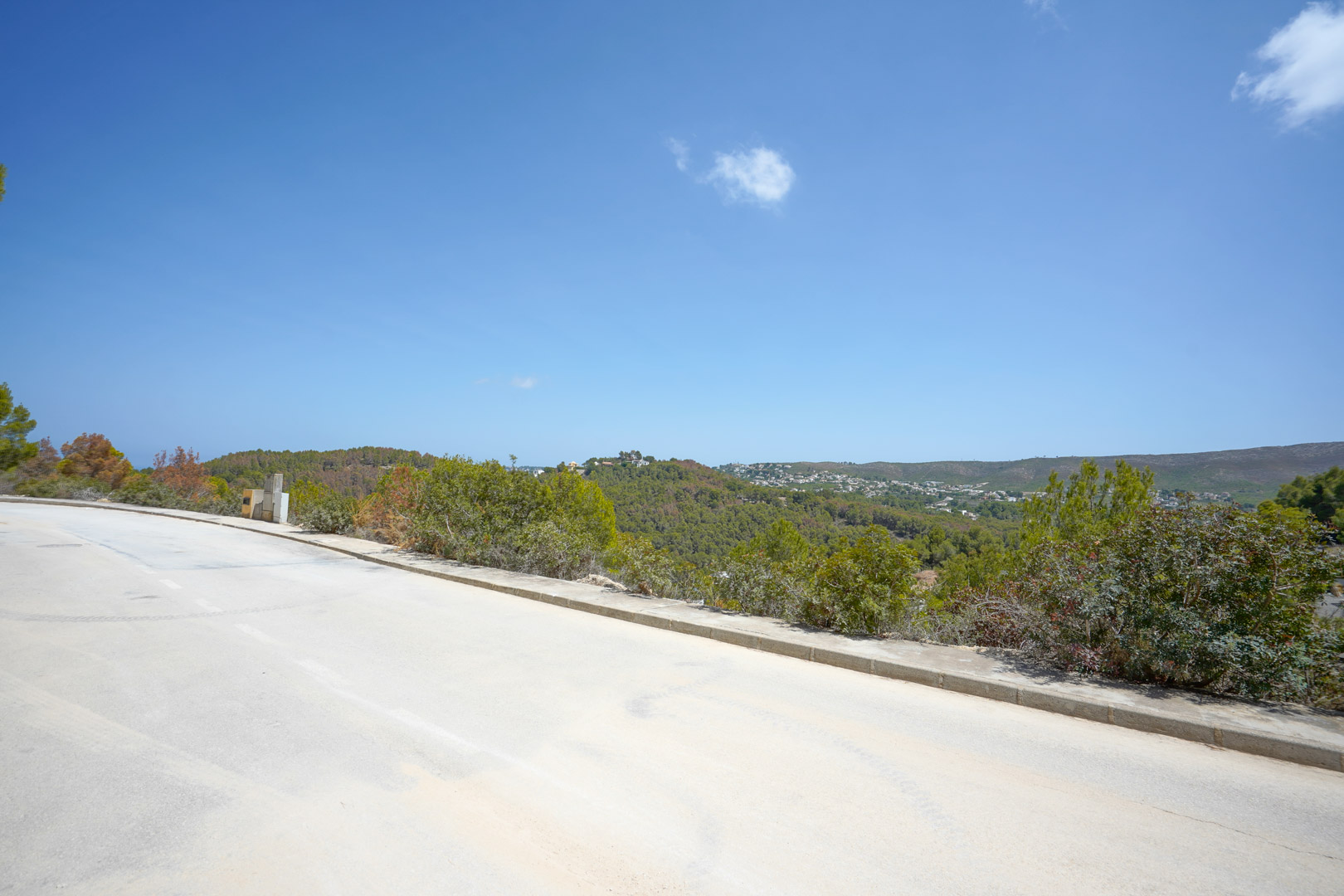 Vista desde la calle asfaltada de la urbanización mostrando el acceso directo a las parcelas y las vistas panorámicas hacia las colinas boscosas.