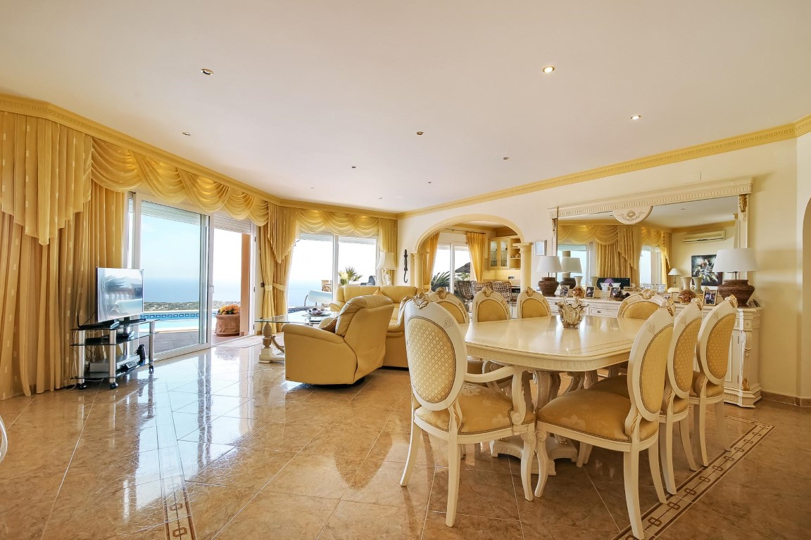 Amplio salón-comedor con suelos de mármol, mobiliario clásico y grandes ventanales que ofrecen vistas panorámicas al mar y acceso directo a la terraza.