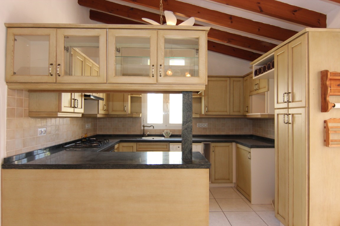 Cocina de estilo rústico con vigas de madera a la vista, encimeras de granito oscuro y armarios con vitrinas. Incluye una práctica barra y techos altos inclinados.