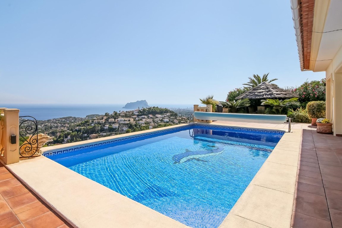 Piscina exterior con mosaico de delfín y vistas panorámicas al mar Mediterráneo y el Peñón de Ifach, rodeada de una amplia terraza de terracota.