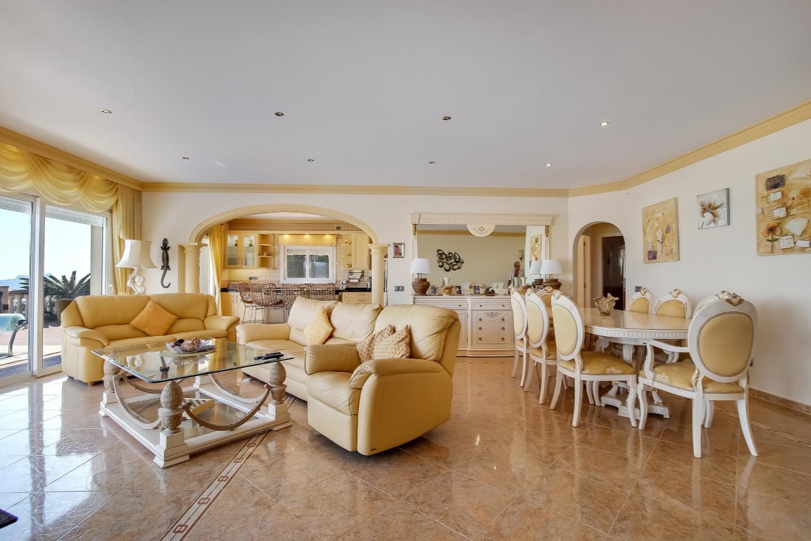 Salón-comedor de planta abierta con suelos cerámicos brillantes, mobiliario clásico en tonos crema y un arco decorativo que conecta con la cocina integrada.