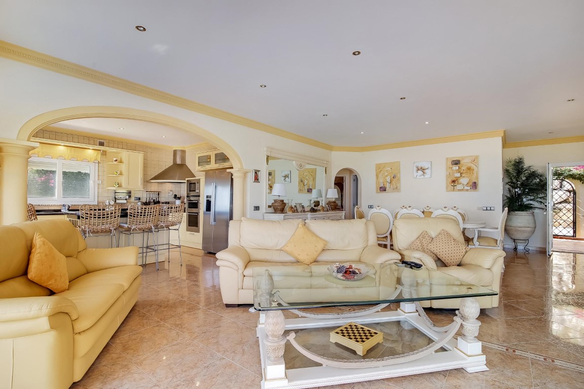 Salón de concepto abierto con sofás de piel, suelos de mármol y un arco decorativo que conecta con la cocina equipada y el comedor formal.