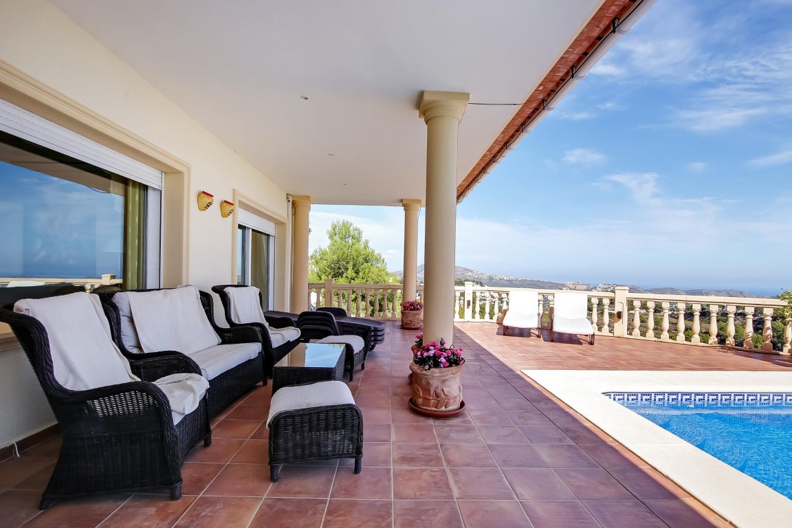 Terraza cubierta con columnas clásicas, mobiliario de mimbre y suelos de terracota junto a la piscina, ofreciendo vistas panorámicas al mar Mediterráneo.