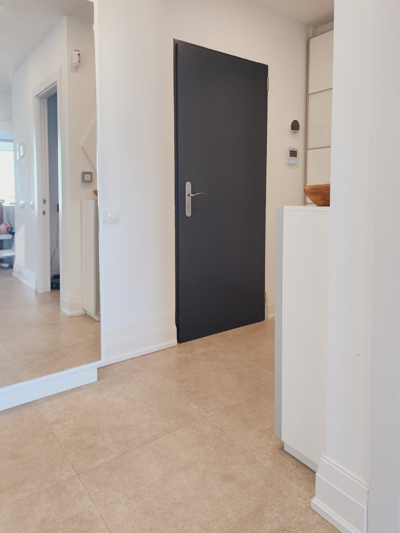 Hall de entrada con suelos de gres porcelánico, gran espejo de cuerpo entero y puerta de diseño en tono oscuro que contrasta con las paredes blancas.