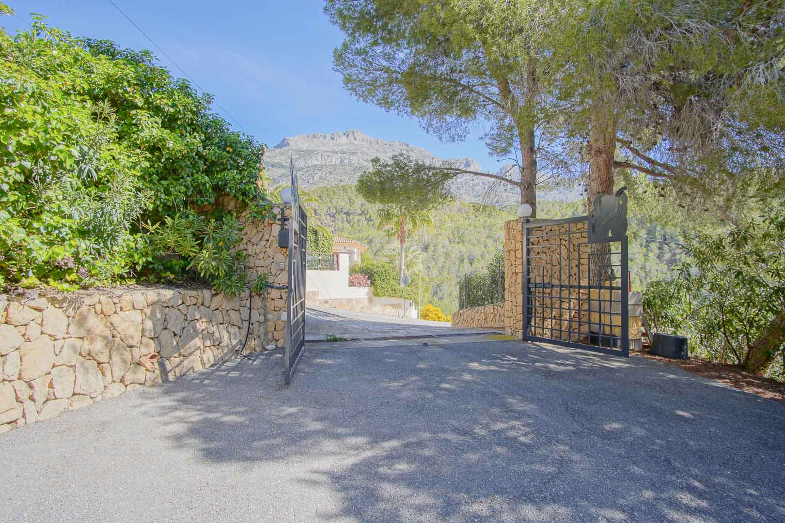 Entrada principal con portón de hierro forjado y muros de piedra natural, ofreciendo vistas despejadas a las montañas y un entorno arbolado privado.