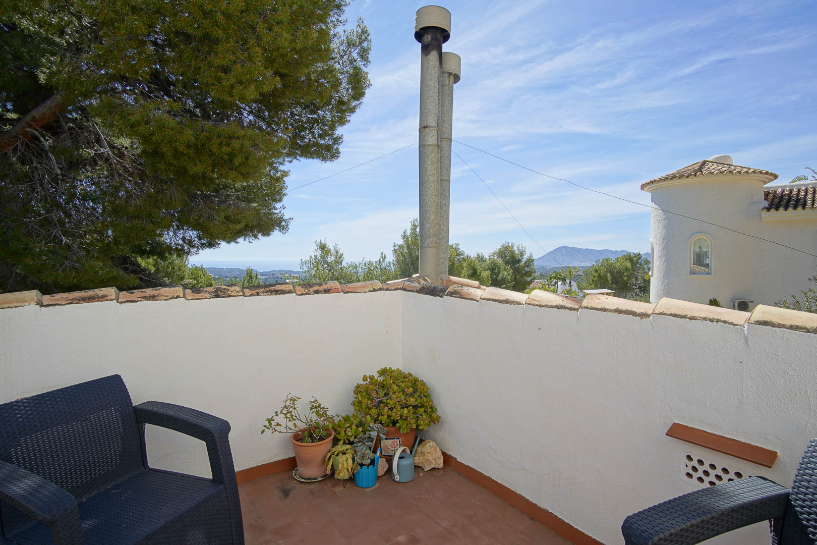 Terraza en planta superior con suelo de barro, mobiliario de exterior y vistas despejadas hacia el mar y la montaña en un entorno rodeado de pinos.