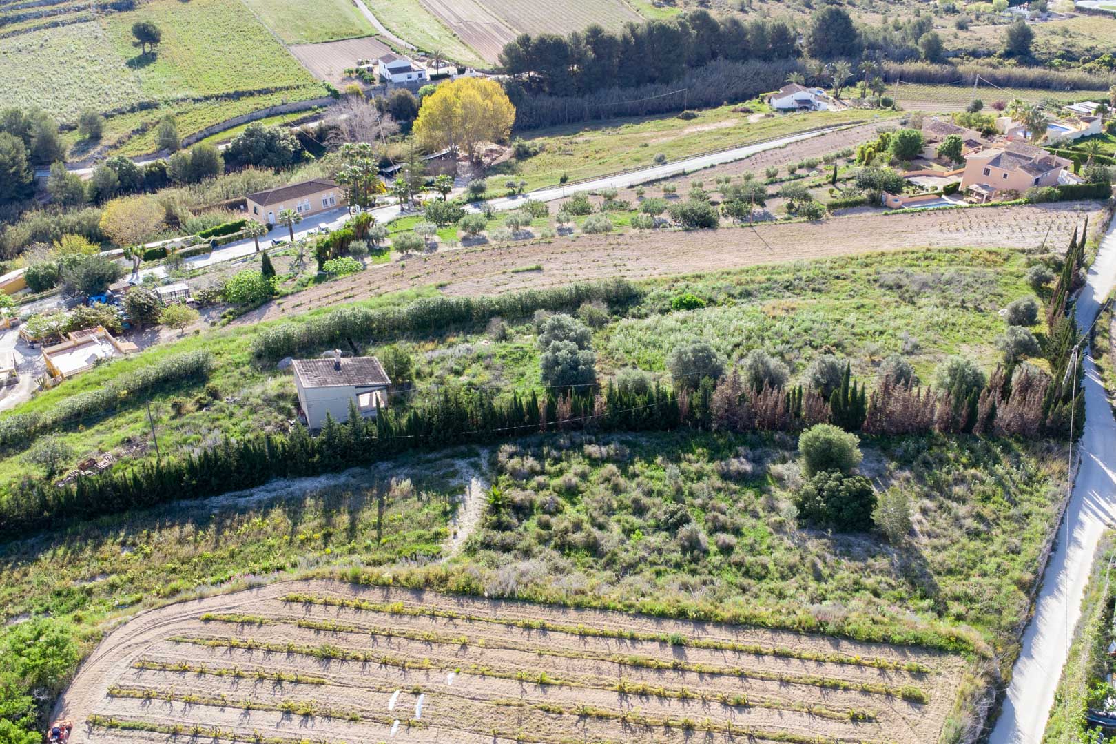 Vista aérea de la amplia parcela rústica en Teulada, mostrando el terreno abancalado con vegetación mediterránea y una pequeña construcción existente.