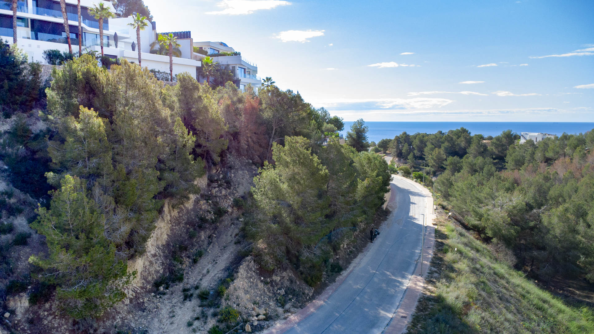 Vista elevada del vial de acceso en Racó de Galeno, destacando la ladera de pinos y las villas modernas con vistas panorámicas al mar Mediterráneo.