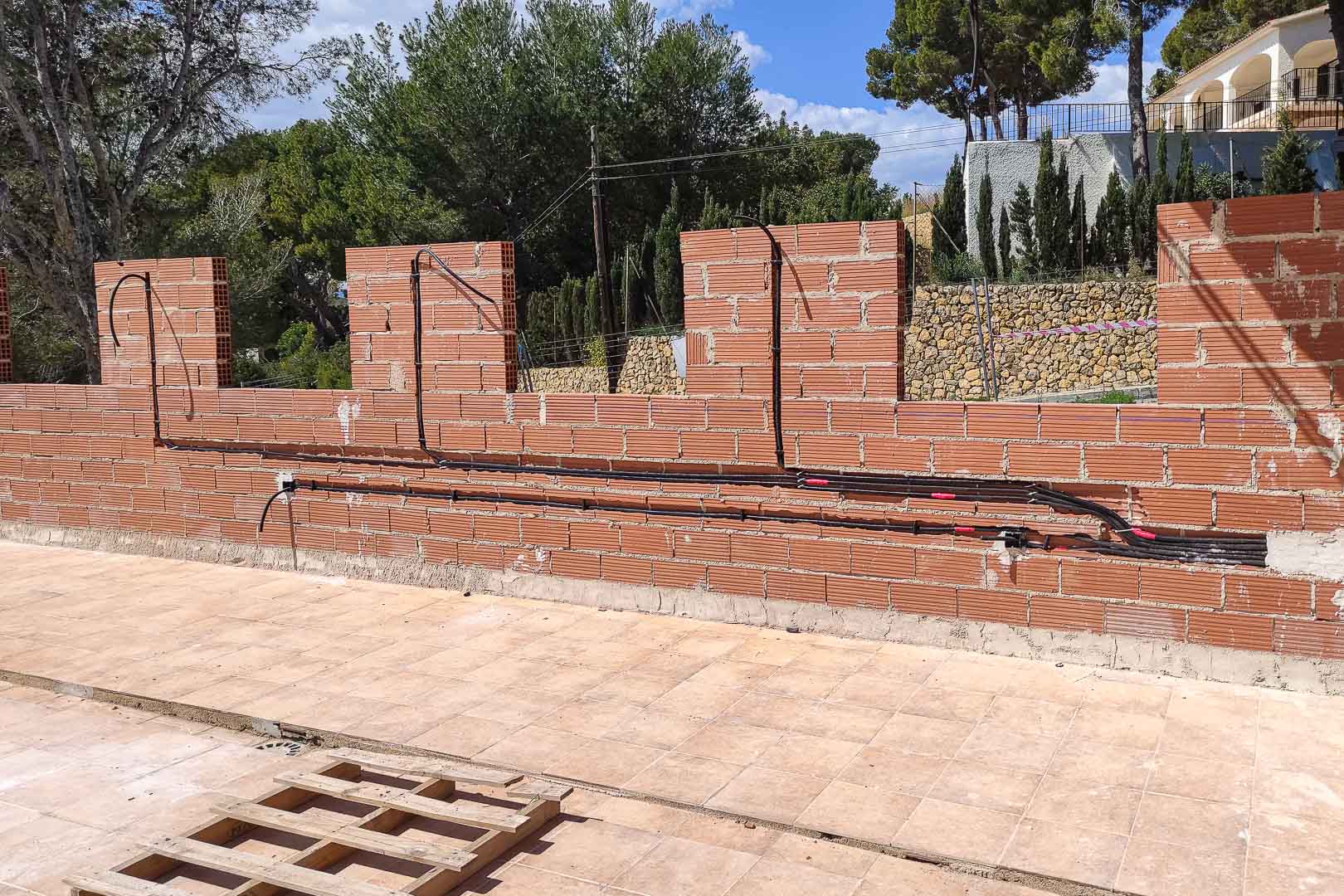 Fase de construcción que muestra la instalación de conductos eléctricos en muros perimetrales de ladrillo, integrando sistemas de seguridad y domótica exterior.