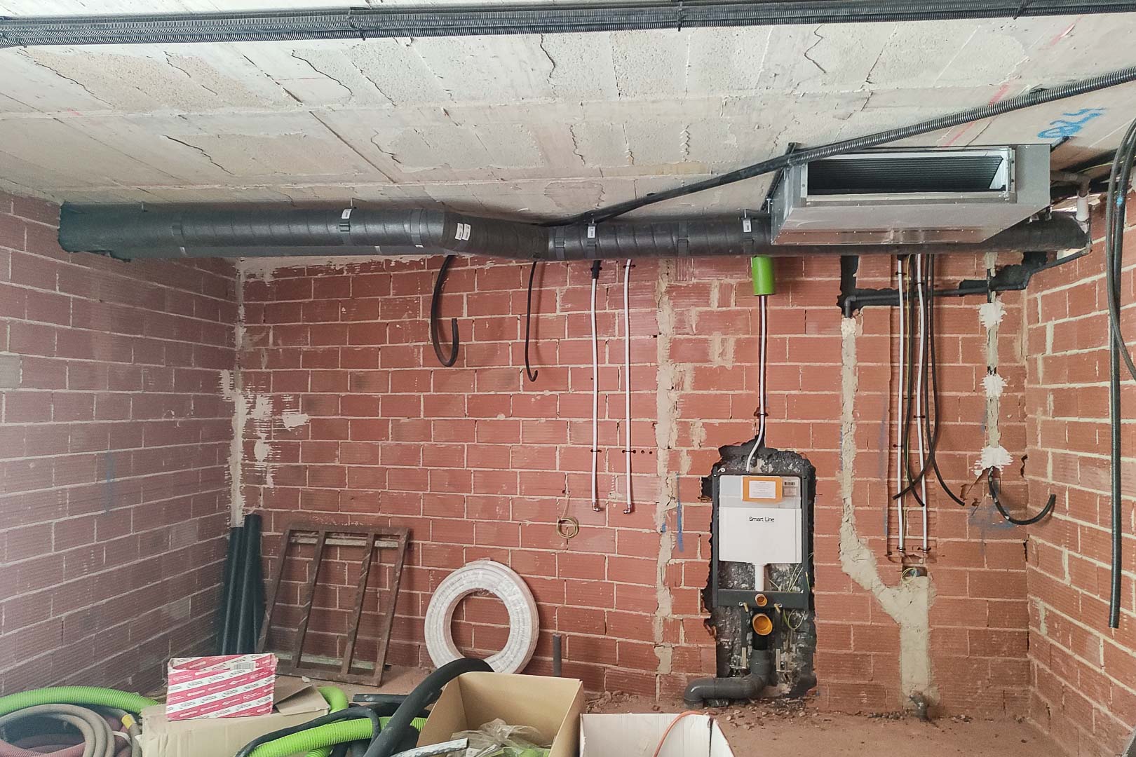 Fase de construcción que muestra la instalación del sistema de climatización por aerotermia y la estructura para sanitario suspendido en tabiquería de ladrillo.