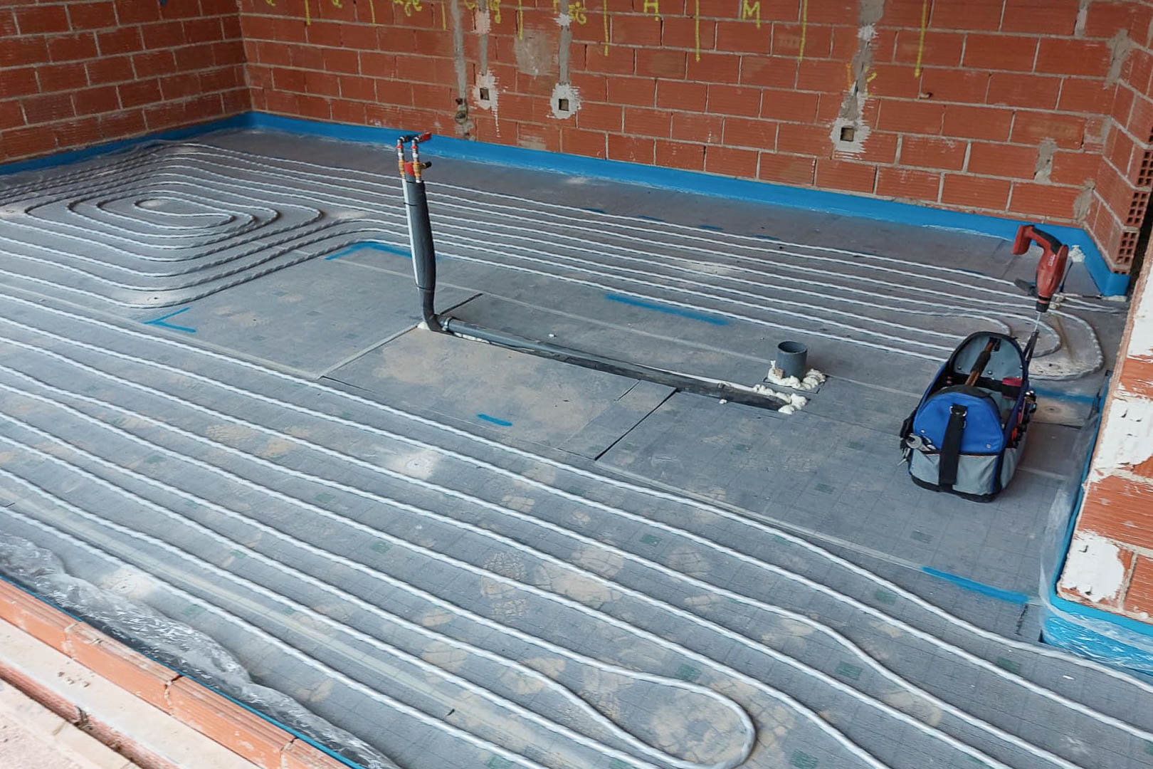 Instalación técnica del sistema de calefacción por suelo radiante, mostrando la distribución de tuberías sobre paneles aislantes en una estancia en fase de obra.