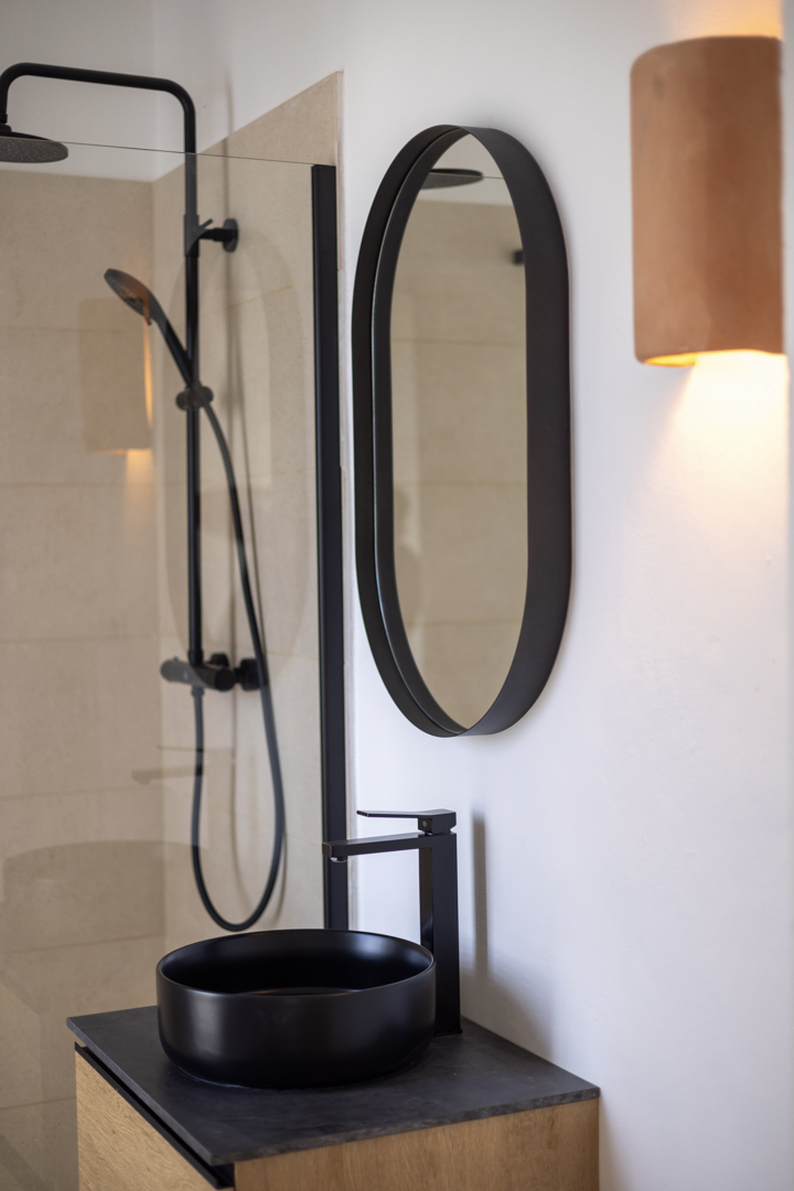 Detalle de baño con lavabo negro circular, espejo ovalado y ducha con mampara.