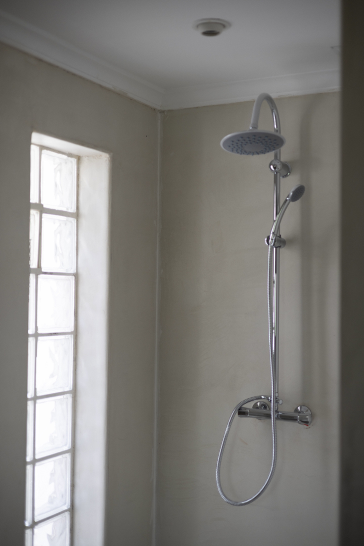Detalle de ducha con rociador y ventana de bloques de vidrio en baño con paredes color crema.