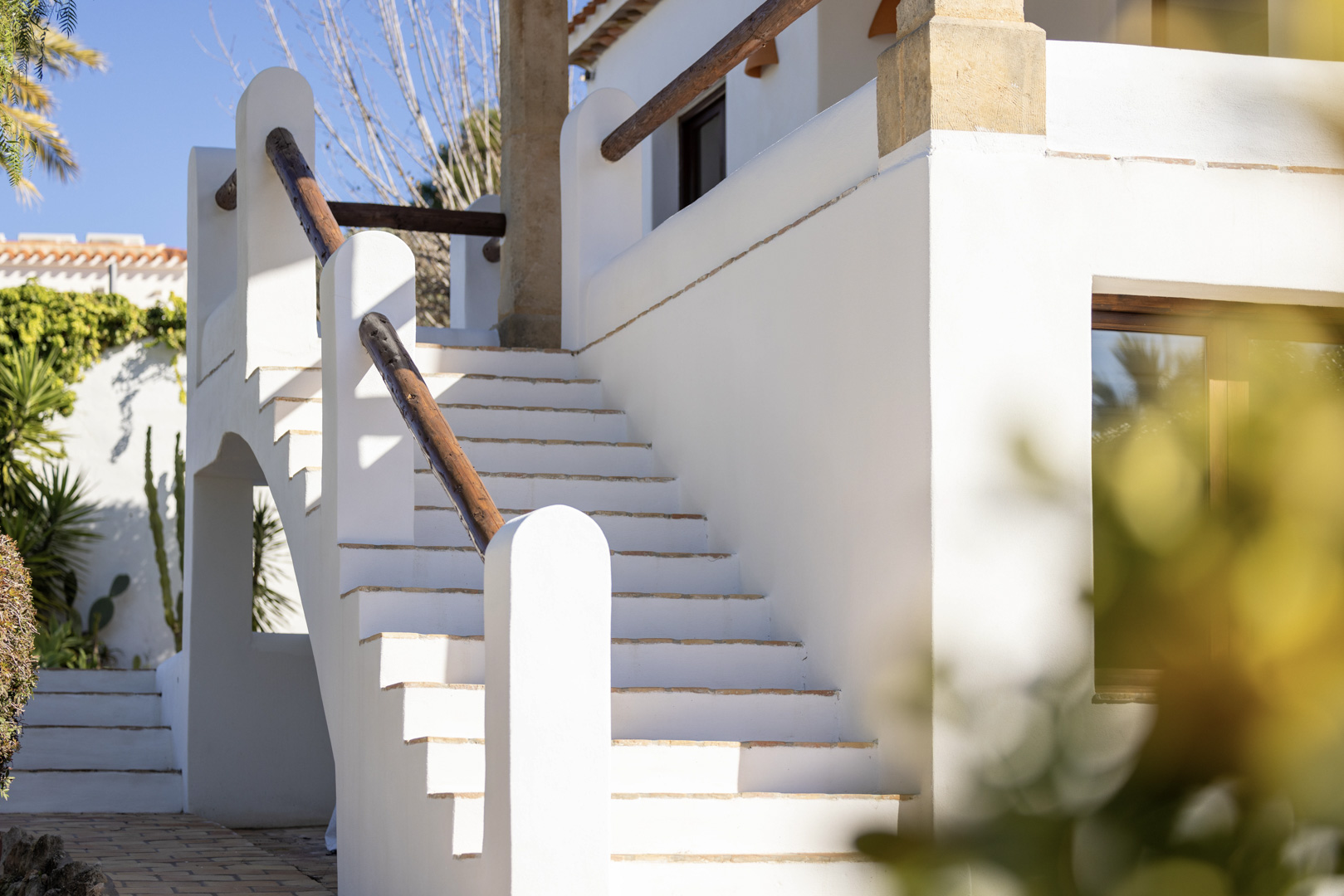 Detalle de escalera exterior blanca con barandilla de madera en villa de Jávea. Diseño mediterráneo luminoso.