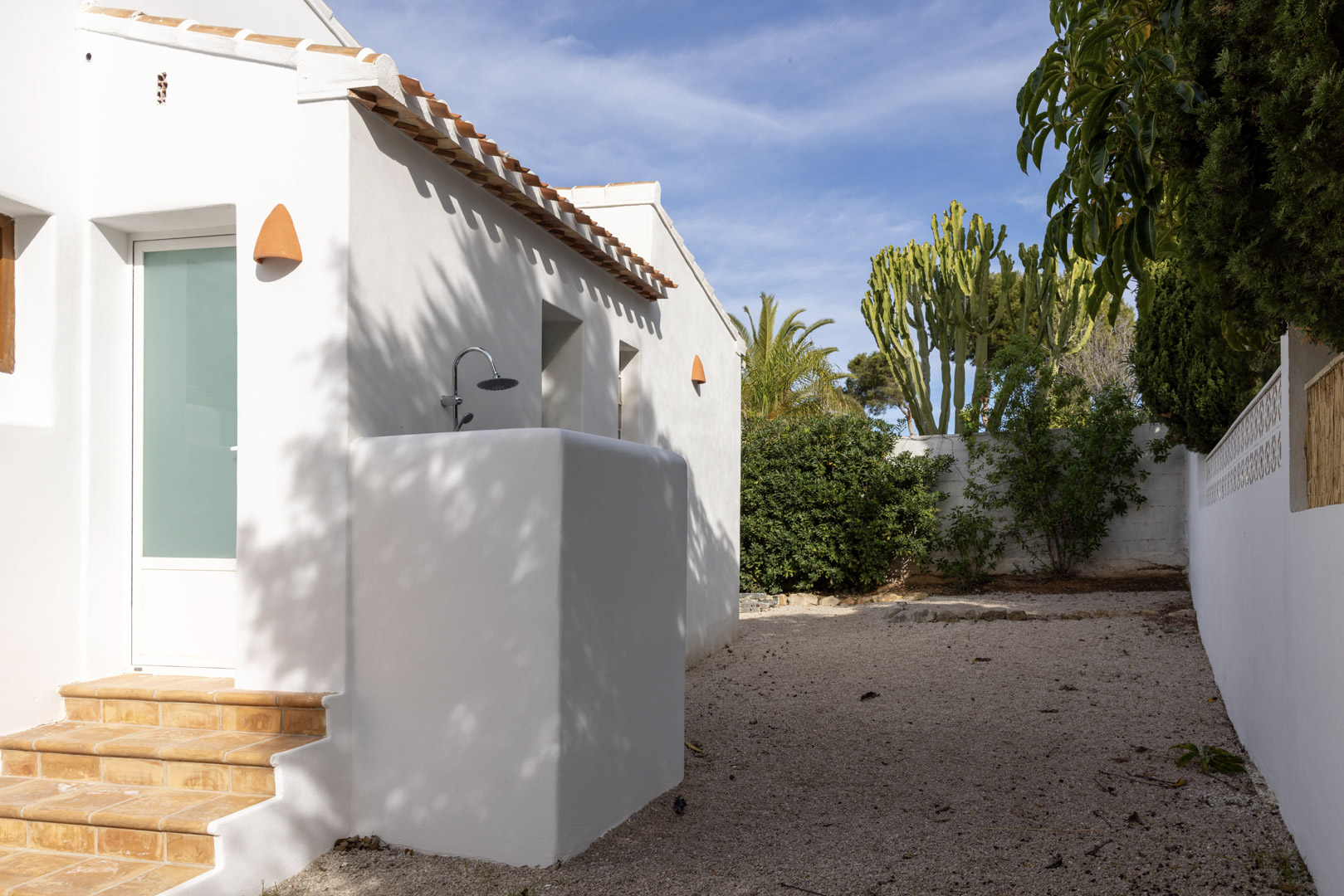 Exterior de la villa con ducha al aire libre y jardín de grava con vegetación variada.