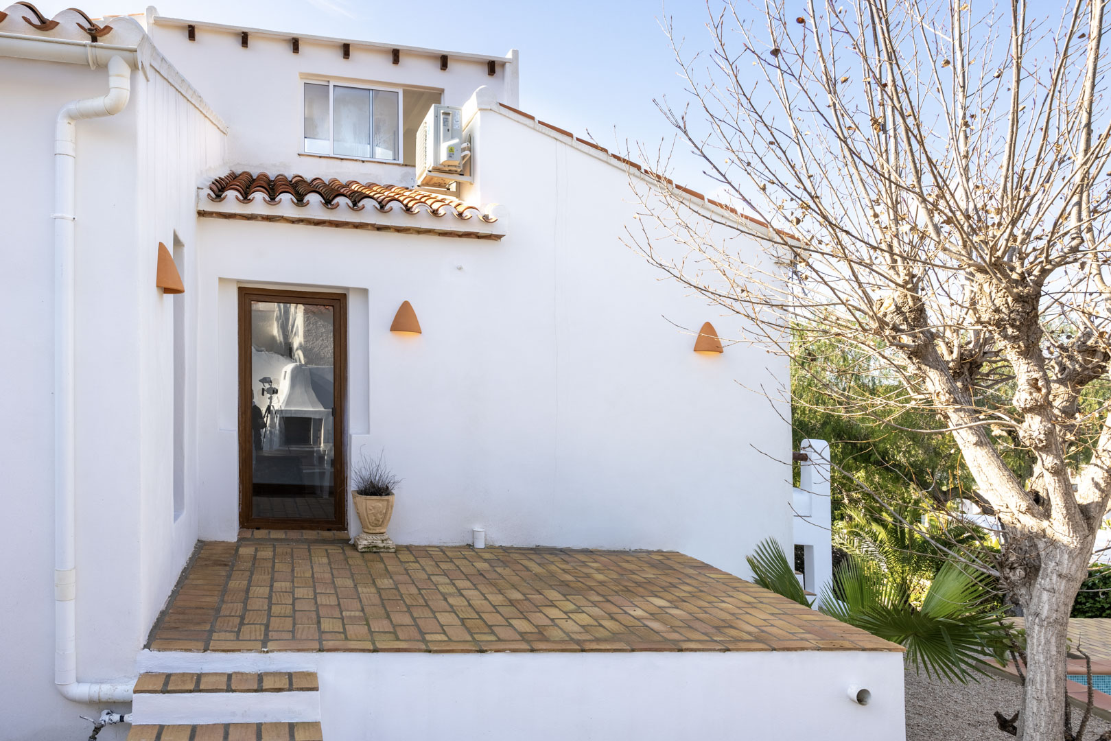 Fachada blanca con terraza de ladrillo y detalles rústicos de iluminación.