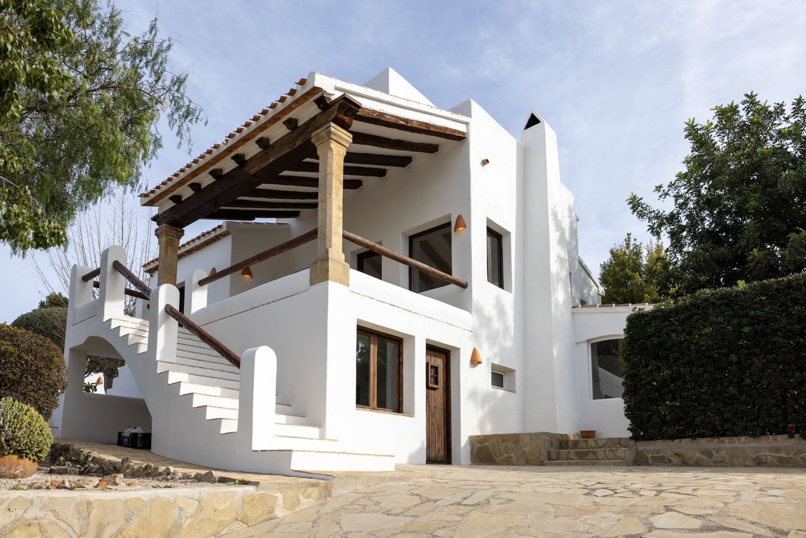 Fachada de villa en Jávea con terraza cubierta, columnas de piedra y acceso por escaleras exteriores.