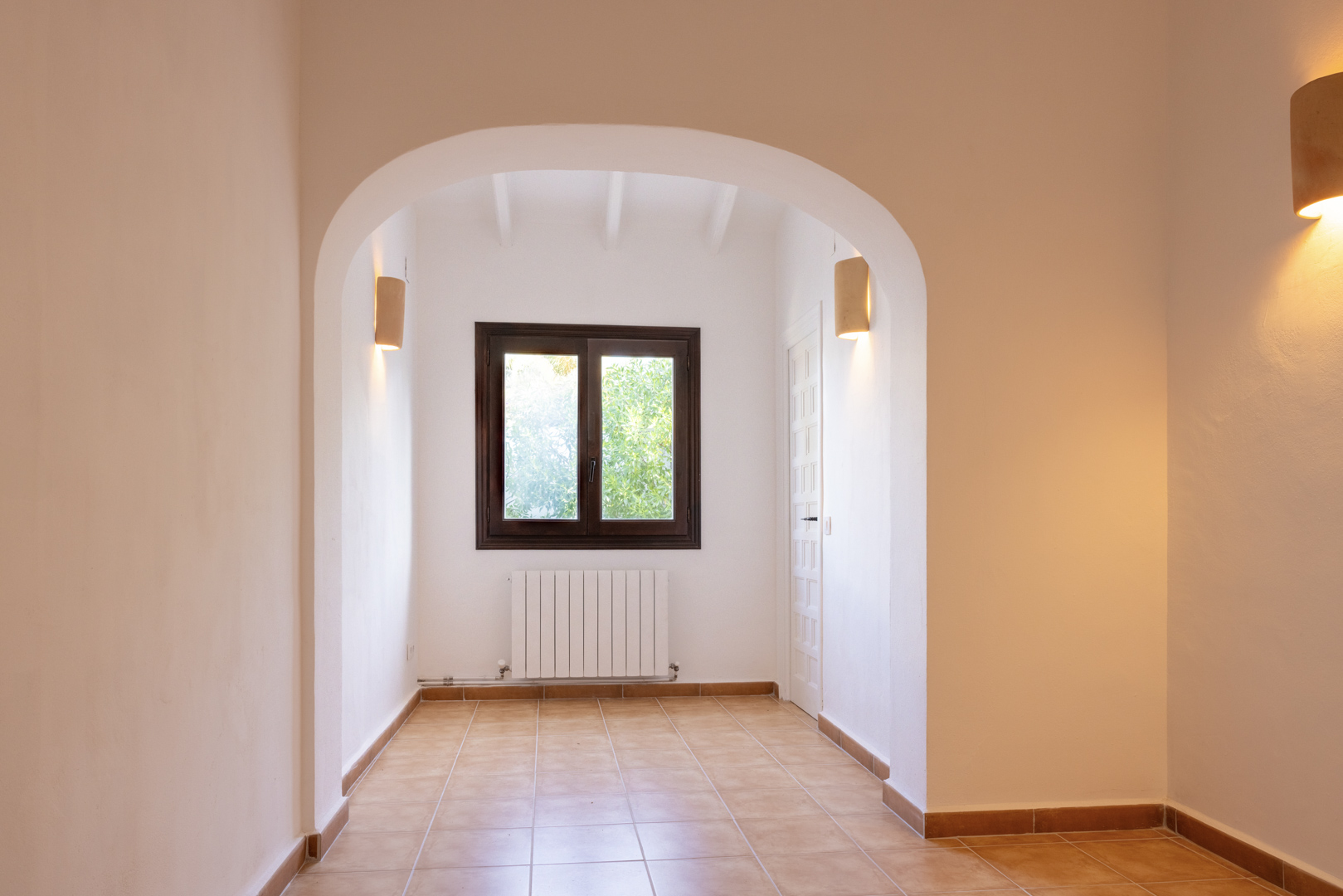 Interior luminoso con arco arquitectónico, suelo cerámico y ventana con carpintería oscura.