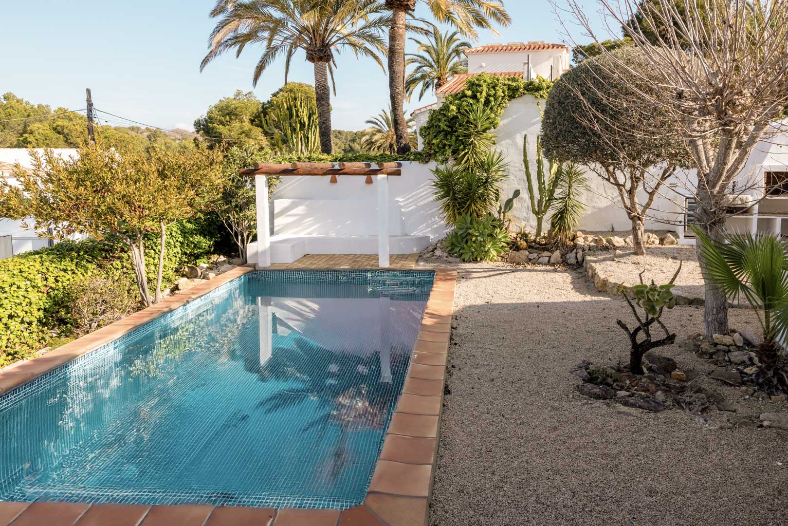 Piscina rectangular con borde de terracota y solárium con pérgola en jardín mediterráneo.