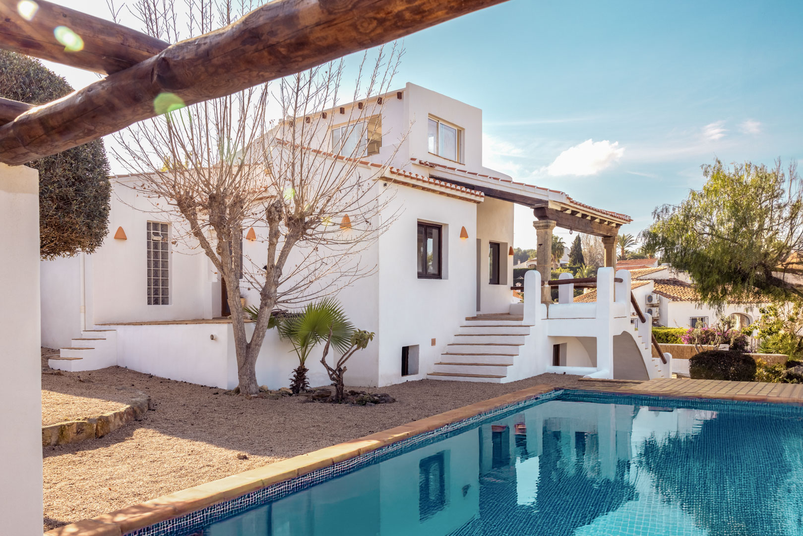 Vista de la villa con piscina azul turquesa y fachada blanca. Diseño mediterráneo con jardín de grava.