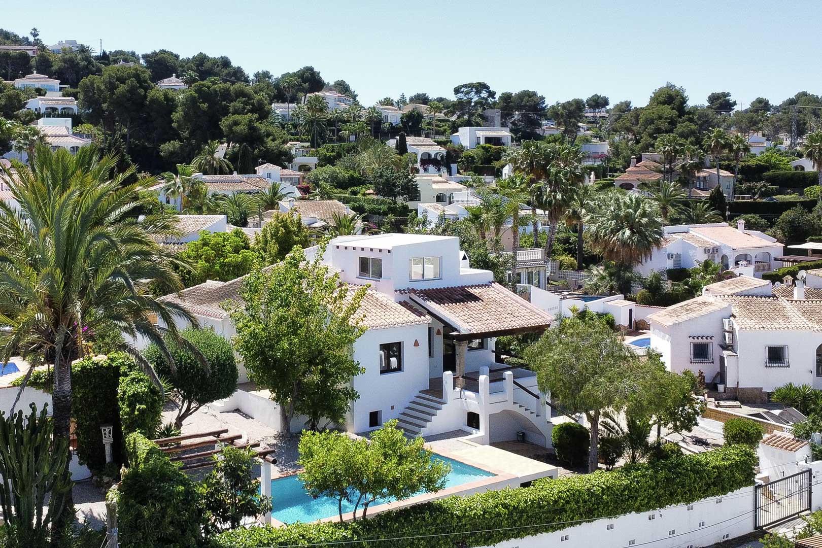 Vista elevada de villa blanca con piscina turquesa y tejado de tejas, rodeada de vegetación en Jávea.