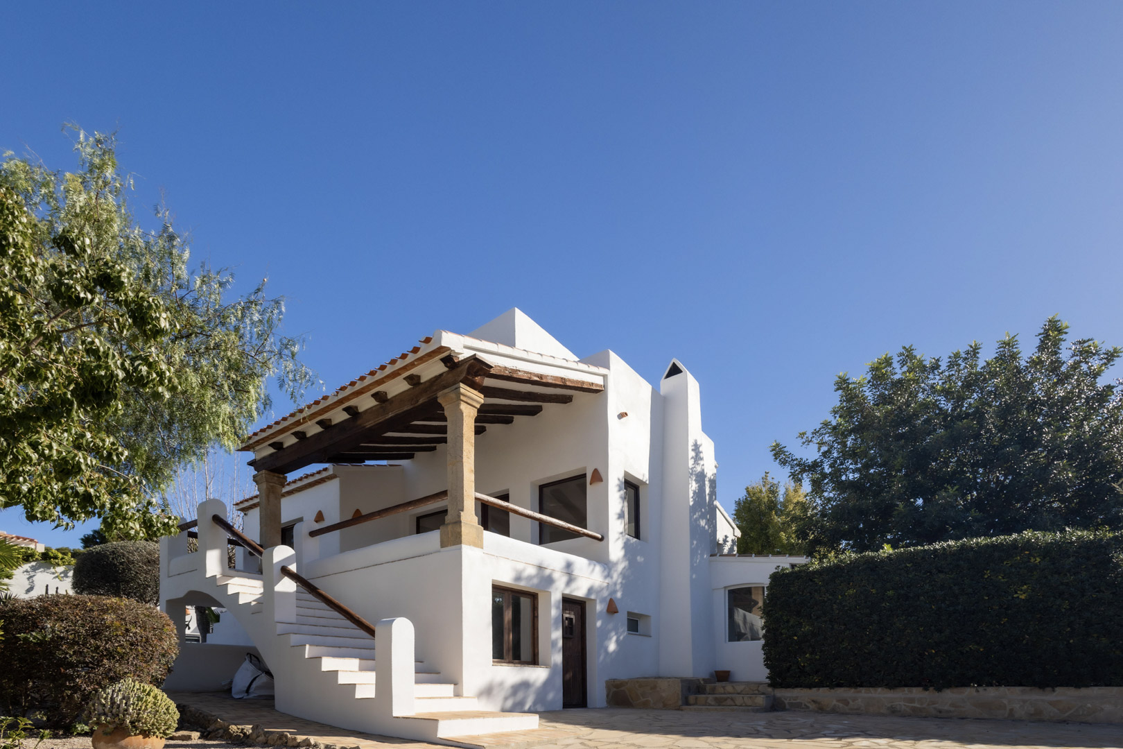 Vista exterior de la villa renovada, destacando la arquitectura tradicional española y la terraza cubierta con vigas de madera.