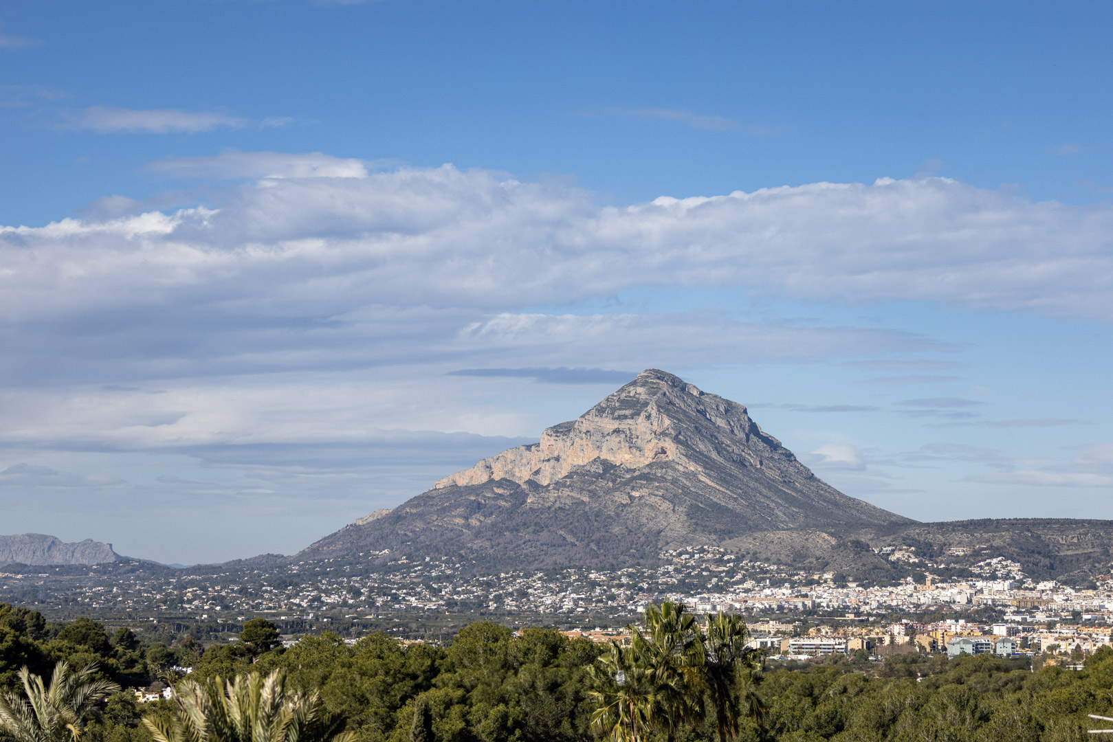 Vista panorámica del Montgó, Jávea, con cielo parcialmente nublado y vegetación en primer plano.